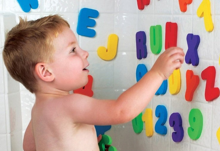 Toddler sticking foam letters to the bath wall